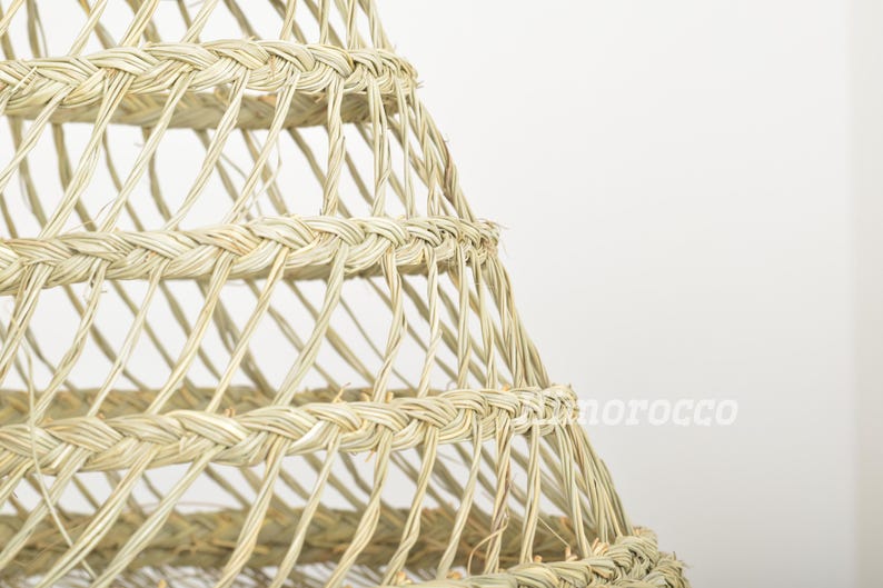 May include: A close-up of a woven lampshade made of natural materials. The lampshade is a light beige color and has a geometric pattern.
