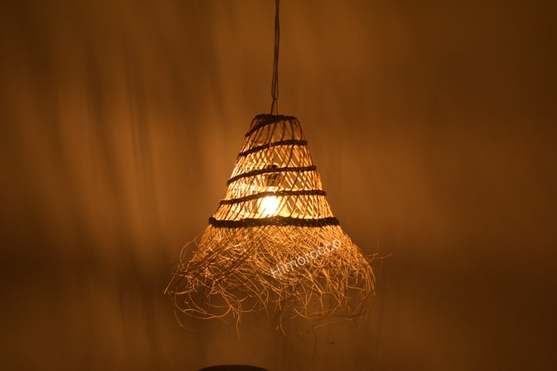 May include: A woven pendant light fixture with a natural, straw-like material. The light is on and casting a warm glow.