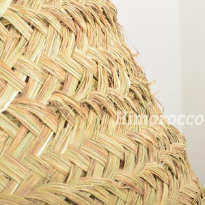May include: Close-up of a woven, light brown, straw lampshade. The lampshade is made of tightly woven strands of straw, creating a textured and intricate pattern.