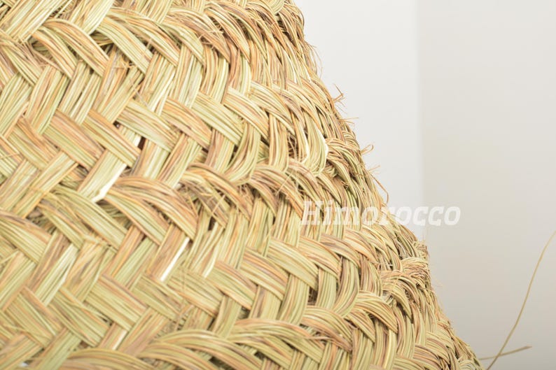 May include: Close-up of a woven, light brown, straw lampshade. The lampshade is made of tightly woven strands of straw, creating a textured and intricate pattern.