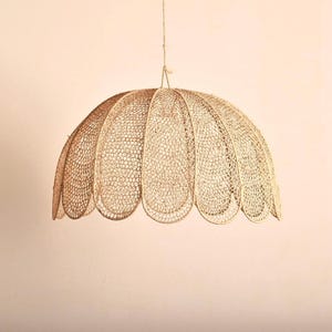 Könnte beinhalten: Eine beige, kuppelförmige Pendelleuchte. Der Lampenschirm besteht aus einem gewebten Material, das ein strukturiertes, offenes Design erzeugt. Das Licht hängt an einem einzigen Kabel und zeigt ein einzigartiges, dekoratives Beleuchtungselement.