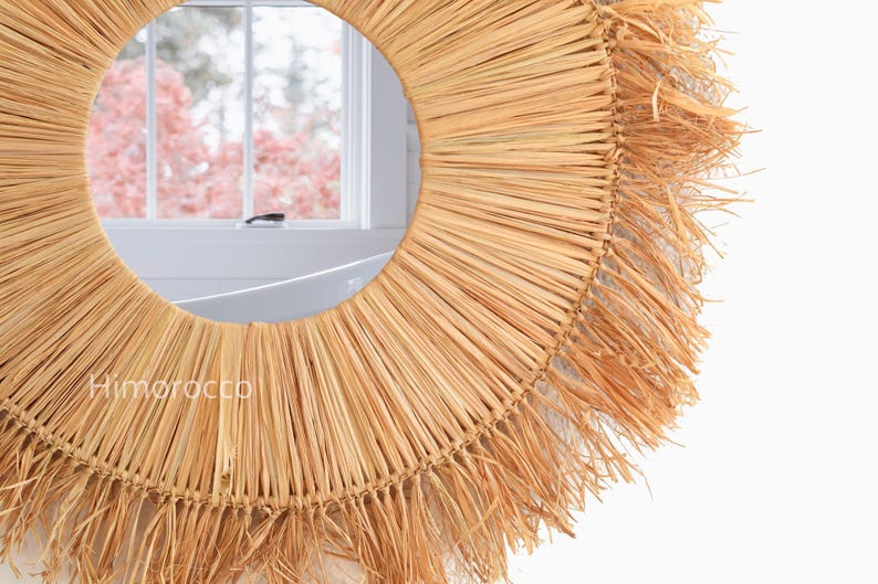 Pu&ograve; includere: Specchio da parete rotondo con cornice in paglia naturale intrecciata. Lo specchio ha un centro in vetro circolare e un design a raggiera. La cornice &egrave; di colore marrone chiaro, con un bordo a frange. Un elemento decorativo per la casa.