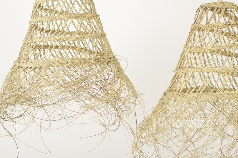May include: Two natural woven pendant light shades with a fringe detail. The shades are made of a light brown material and have a conical shape.