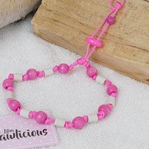 Op de afbeelding: Roze en witte kralen hondenhalsband met een roze verstelbaar koord. De halsband heeft een roze plastic sluiting. De halsband ligt op een wit pluche oppervlak.