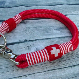 Op de afbeelding: Rood en wit gestreept touwhalster met een zilveren clip en een rood Zwitserse kruis patch.