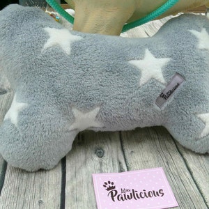 Op de afbeelding: Een grijze pluche hondenbot met witte sterren. Het bot heeft een label met de tekst "Pawlicious".
