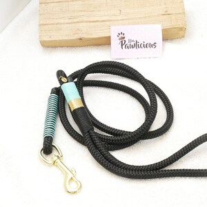 Op de afbeelding: Zwarte touwhalster voor honden met een turquoise en gouden accent. De halster heeft een gouden metalen clip.
