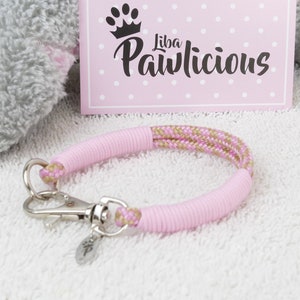 Op de afbeelding: Roze en gouden touwhalster met een zilveren sluiting. Het halster ligt op een wit, pluche oppervlak. De tekst "Liba Pawlicious" is zichtbaar op een roze kaart op de achtergrond.