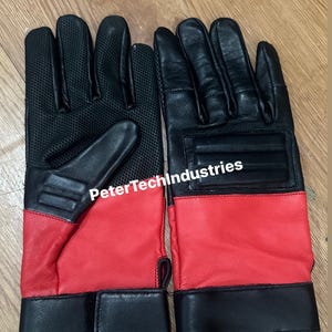 Può includere: Un paio di guanti in pelle nera con dettagli rossi e un cinturino da polso nero. I guanti hanno un pannello in rete sul retro della mano e il testo "PeterTechIndustries" è stampato sul retro del guanto destro.