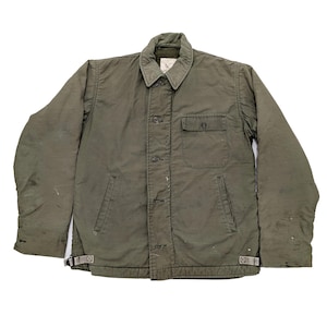 May include: Olive green military-style jacket with a button-up front, a collared neckline, and a single chest pocket. The jacket has two side pockets and adjustable straps at the waist. The jacket is approximately 30 inches long.