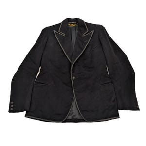 以下が含まれることがあります： グレーのトリムがラペル、ポケット、エッジを縁取る黒のブレザー。 ブレザーはシングルボタン留めで、各袖口に3つのボタンが付いています。 内側の裏地は襟とポケットに見えます。