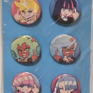 Op de afbeelding: Set van zes ronde pins met anime-achtige illustraties van personages met verschillende haarkleuren en uitdrukkingen. Elke pin toont een personage dat de middelvinger opsteekt. De pins zijn verpakt op een blauwe achtergrond.