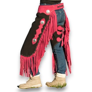 Può includere: Chaps in pelle nera e rosa con frange. Le chaps hanno un design decorativo e vengono indossate sopra i jeans.