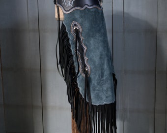 May include: A pair of blue suede chaps with black fringe and a black leather belt with the initials "KM" embroidered on it.