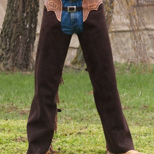 Pu&ograve; includere: Chaps in pelle marrone con frange e una cintura con fibbia. I chaps hanno un design decorativo sul davanti con le iniziali "MV".