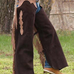 Pu&ograve; includere: Chaps in pelle marrone con dettagli a frangia e un design lavorato. Le chaps hanno una chiusura a fibbia e vengono indossate sopra i jeans.
