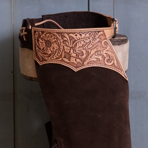 Pu&ograve; includere: Chaps in pelle marrone con un design floreale decorativo. I chaps hanno una cintura con fibbia e sono realizzati in pelle morbida e flessibile.