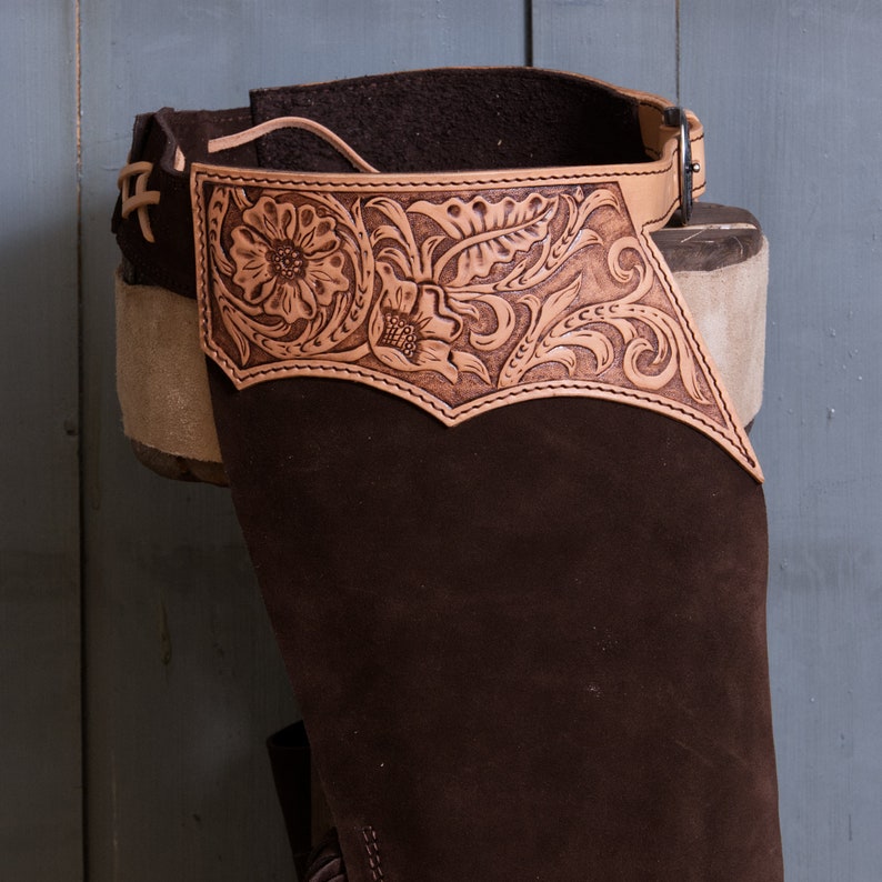 Pu&ograve; includere: Chaps in pelle marrone con un design floreale decorativo. I chaps hanno una cintura con fibbia e sono realizzati in pelle morbida e flessibile.