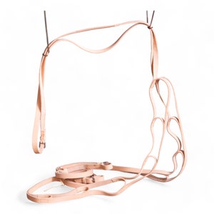 May include: A light tan leather horse bridle with multiple straps and buckles. The bridle is suspended from above, showcasing its intricate design and craftsmanship. The leather appears to be of high quality, with a natural finish.