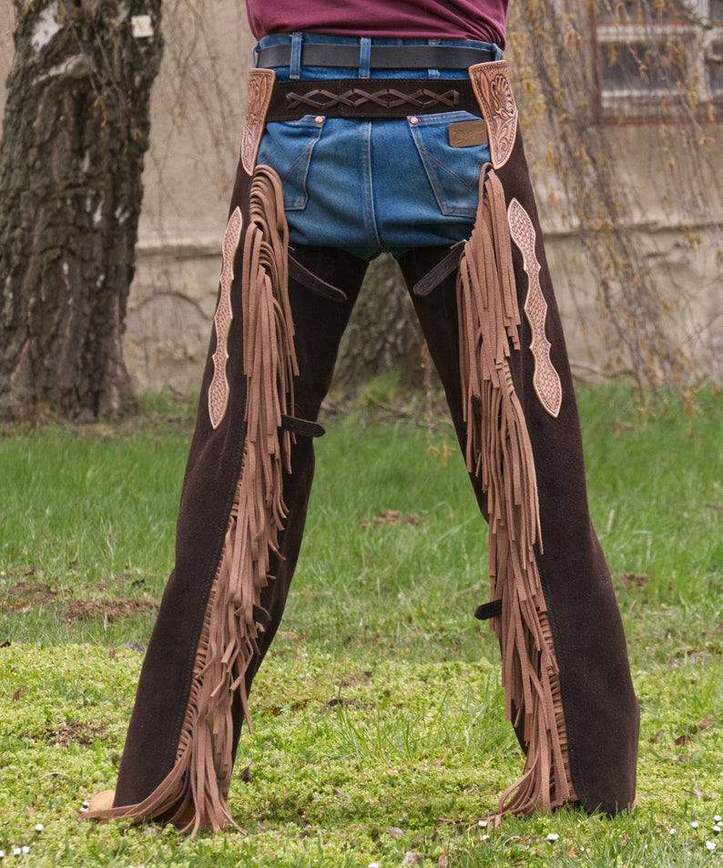 Pu&ograve; includere: Chaps in pelle marrone con frange e cintura. I chaps hanno un design decorativo sul lato.