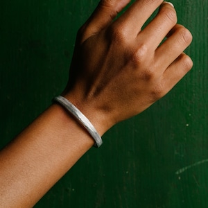 Peut inclure: Un bracelet en argent martelé sur le poignet d'une personne sur un fond vert.