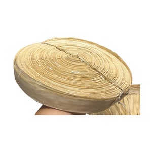 May include: A rolled bundle of natural-colored, dried palm leaves, tightly bound with twine. The circular arrangement of the leaves creates a spiral pattern. The leaves have a light tan color and a slightly textured appearance.