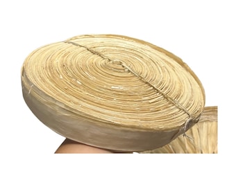 Pode incluir: Um rolo de folhas de palmeira secas de cor natural, firmemente amarradas com barbante. A disposição circular das folhas cria um padrão em espiral. As folhas têm uma cor castanho-clara e uma aparência ligeiramente texturizada.