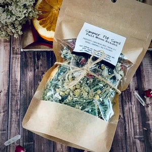 May include: A brown paper bag with a clear plastic window containing a simmer pot spell for a full moon ritual. The ingredients include lemon balm, mint, yarrow, orange, chamomile, sage, and rosemary. The bag is tied with twine and has a label that reads "Simmer Pot Spell Full Moon Ritual".