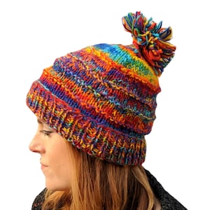 May include: A colorful knitted beanie with a rainbow pattern and a fluffy pom pom on top.