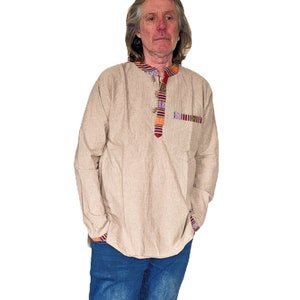 May include: A beige long-sleeved shirt with a colorful patterned band around the collar and a matching pocket on the left side. The shirt has a button-up front.