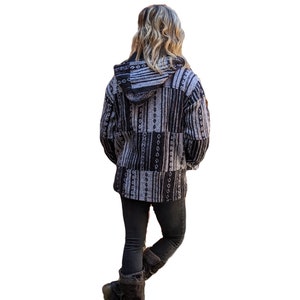 K&ouml;nnte beinhalten: Eine schwarze und wei&szlig;e gemusterte Kapuzenjacke mit Rei&szlig;verschluss. Die Jacke ist aus weichem, flauschigem Material und hat eine lockere Passform.