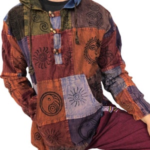 May include: A multi-coloured patchwork hoodie with sun and yin-yang symbols. The hoodie features a drawstring hood, wooden toggle buttons, and a front pocket. The colour palette includes orange, red, blue, and green. The sleeves and body are made of various fabric squares.