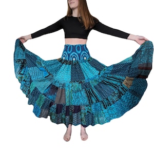 May include: A woman wearing a black long-sleeved top and a blue and green patchwork skirt with a ruffled hem. The skirt is very full and flowing.