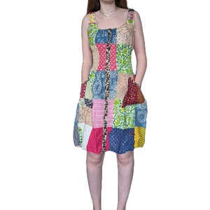 May include: A patchwork dress with a variety of floral and geometric patterns in shades of pink, blue, green, yellow, and brown. The dress has a sleeveless design and a fitted bodice with a button-up front.