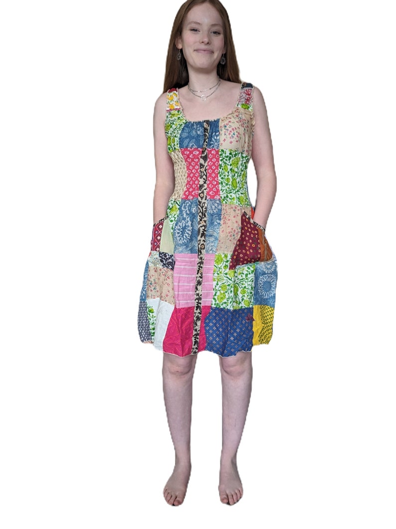 May include: A patchwork dress with a variety of floral and geometric patterns in shades of pink, blue, green, yellow, and brown. The dress has a sleeveless design and a fitted bodice with a button-up front.