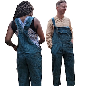 May include: Two people wearing dark blue denim overalls. The person on the left is wearing a white vest top and has long, dark hair. The person on the right is wearing a light brown shirt.