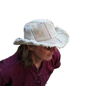 May include: A white crocheted hat with a frayed brim and colourful stitching. The hat is made from recycled materials and has a unique, bohemian style.