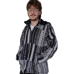 May include: A black and white patterned zip-up jacket with a hood. The jacket has a geometric design with stripes and a patchwork look.