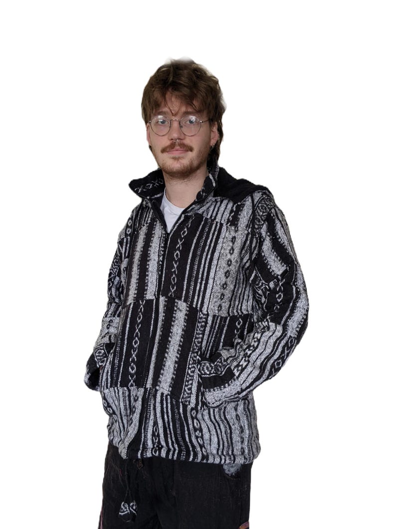 K&ouml;nnte beinhalten: Eine schwarze und wei&szlig;e gemusterte Jacke mit Rei&szlig;verschluss und Kapuze. Die Jacke hat ein geometrisches Design mit Streifen und einem Patchwork-Look.