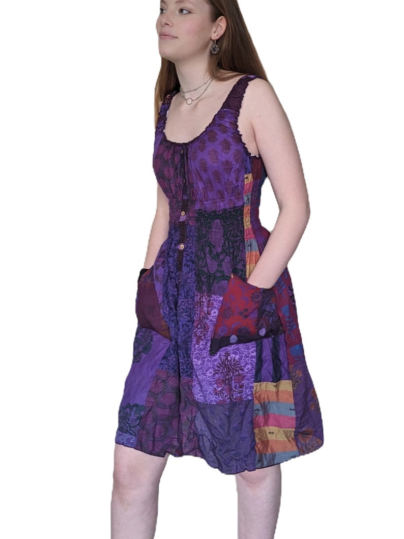 May include: A purple patchwork dress with a scoop neck and a button closure. The dress has a fitted bodice and a flowy skirt with pockets.