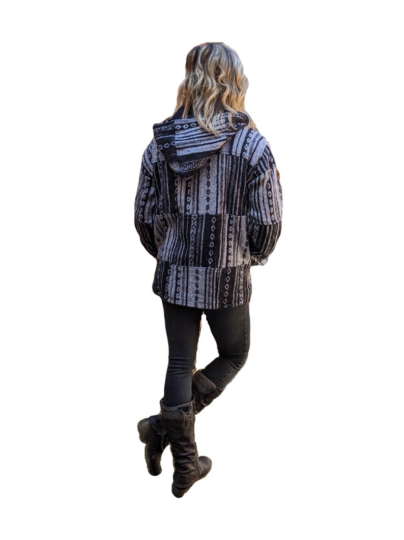 K&ouml;nnte beinhalten: Eine schwarze und wei&szlig;e gemusterte Kapuzenjacke mit Rei&szlig;verschluss. Die Jacke ist aus weichem, flauschigem Material und hat eine lockere Passform.