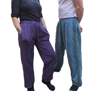 May include: Two pairs of casual trousers. One pair is purple with vertical stripes, the other is blue and green striped. Both have a drawstring waist and pockets. The trousers are worn with a black top and a white t-shirt.