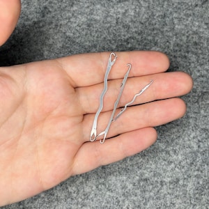 May include: Three silver crochet hooks with different shaped ends. The hooks are lying on a person's hand.