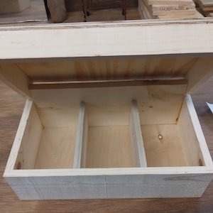 May include: A wooden box with a hinged lid and three compartments inside. The box is made of light-colored wood and has a natural finish.
