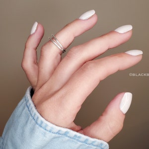May include: A hand with white nail polish is wearing a silver ring on the middle finger. The hand is wearing a light blue denim shirt.