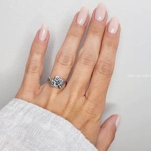 May include: A silver ring with a floral design. The ring is on a person's finger, and their nails are painted a light pink color.
