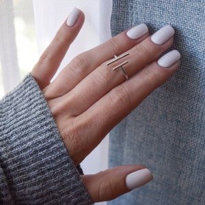 May include: A silver ring with a geometric design. The ring is on a finger with white nail polish.