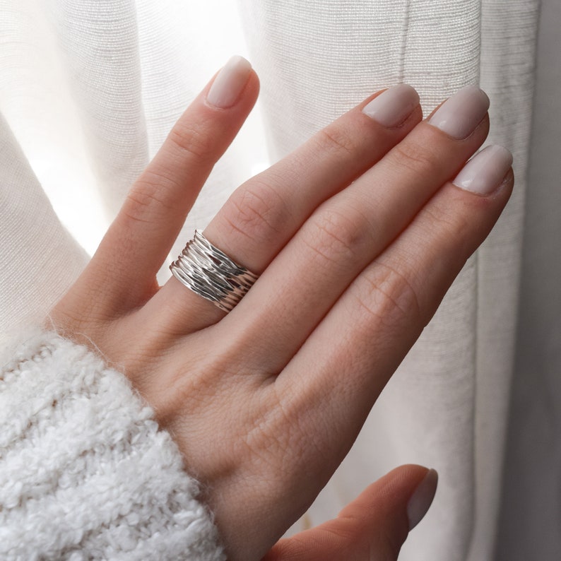 May include: A silver ring made of multiple thin bands twisted together. The ring is worn on a person's finger.