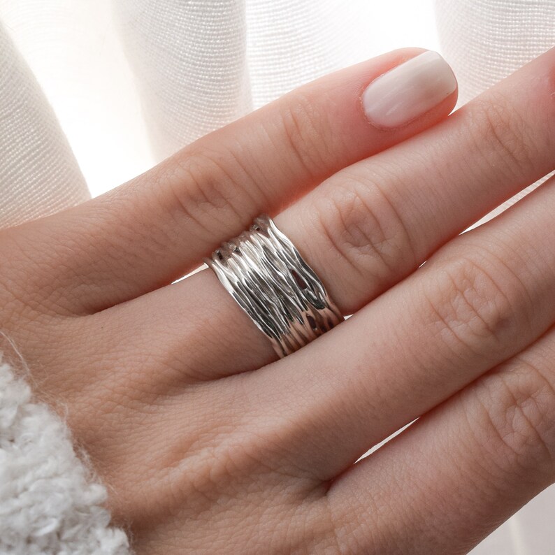 May include: A silver ring with a textured, woven design. The ring is stacked with multiple bands.