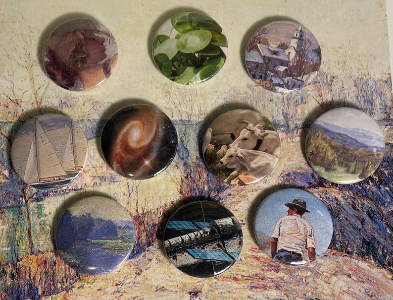 May include: Nine round, colourful buttons with various images, including a sailboat, a galaxy, a landscape, a church, a plant, a group of cows, a man in a hat, and a blue and black abstract design.